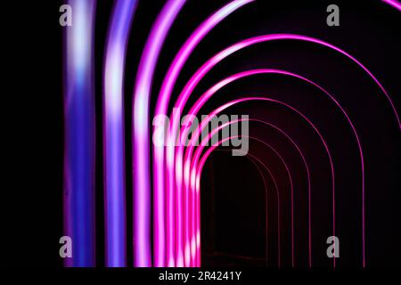 Unendliche Korridore mit schwarzem Hintergrund und leuchtend pinkfarbenen und violetten Torbögen Stockfoto