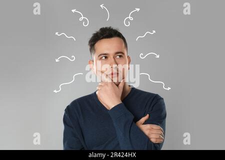 Berufswahl oder andere Lebensbereiche, Konzept. Ich treffe Entscheidungen, ein aufmerksamer junger Mann, umgeben von gezeichneten Pfeilen auf grauem Hintergrund Stockfoto