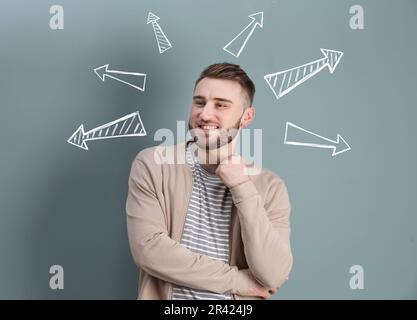 Berufswahl oder andere Lebensbereiche, Konzept. Entscheidungen treffen, junger Mann, umgeben von gezeichneten Pfeilen auf grauem Hintergrund Stockfoto