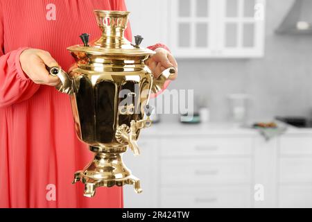 Eine Frau, die einen traditionellen russischen Samowar in der Küche hält, Nahaufnahme. Platz für Text Stockfoto