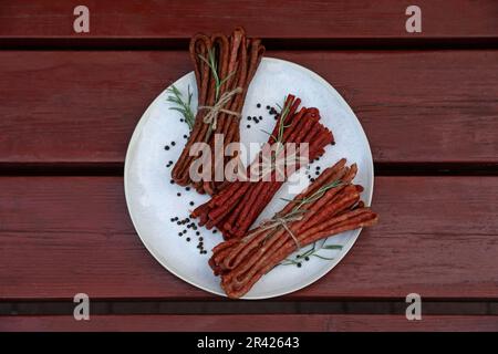 Leckere trocken gepökelte Würstchen (kabanosy) und Gewürze auf Holztisch, Draufsicht Stockfoto