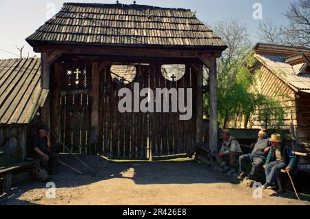 Maramures, Rumänien, 2001. Einheimische Männer, die sich an einem großen traditionellen Holztor unterhalten. Stockfoto