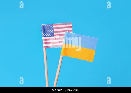 Kleine Papierflaggen der Ukraine und der USA auf hellblauem Hintergrund Stockfoto