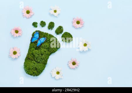 Kreative Öko, Umweltschutz, Earth Day Konzept. Barfußabdruck aus natürlichem grünen Moos, Blumen und Schmetterlingen auf blu Stockfoto