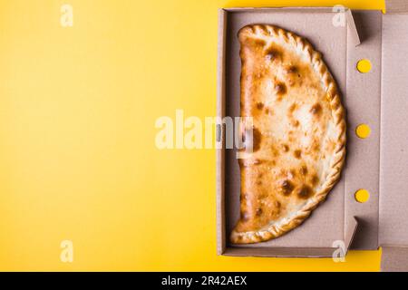 Geschlossene Pizza-Calzone in Packbox auf gelbem Hintergrund Stockfoto