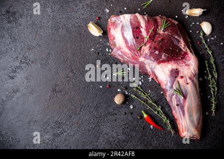 Rohes frisches Lammfleisch mit Schaft und Gewürzen auf schwarzem Steinhintergrund Stockfoto