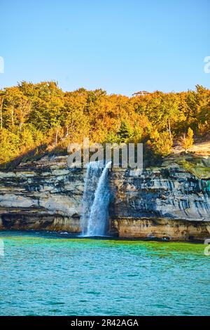 Sommerwald hinter einem hohen Wasserfall, der in den See oder das Meer fließt, mit Pictured Rocks im Nationalpark Stockfoto