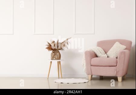 Gemütlicher Sessel und Vase mit Pampasgras auf dem Couchtisch an der weißen Wand Stockfoto