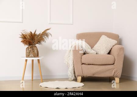 Gemütlicher Sessel und Vase mit Pampasgras auf dem Couchtisch an der weißen Wand Stockfoto