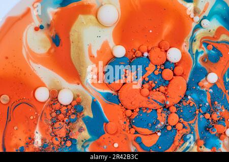Horizontaler abstrakter Tanz der Öllache von goldener Creme mit orangefarbener und blauer Acrylfarbe im Hintergrund Stockfoto