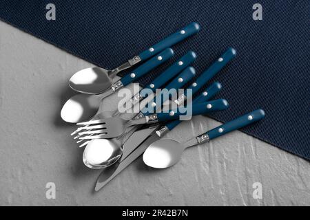 Besteckset aus Edelstahl mit blauen Griffen auf grauem Hintergrund Stockfoto