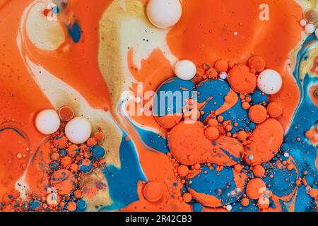 Horizontaler abstrakter Schmetterling des Ölflusses aus goldener Creme, die mit orangefarbener und blauer Acrylfarbe im Hintergrund vermischt wird Stockfoto