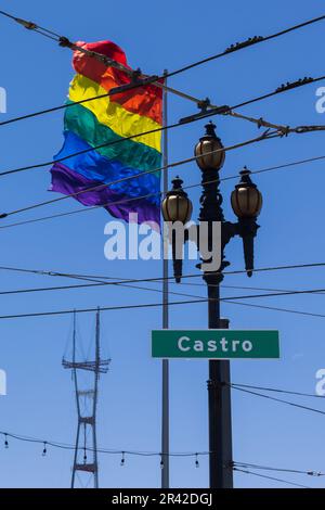 Große, lebendige Regenbogenflagge mit blauem Himmel und Schild auf der Castro Street. Das Castro-Viertel, San Francisco. Mehrfarbige Fahne flattert im Wind auf einem Su Stockfoto