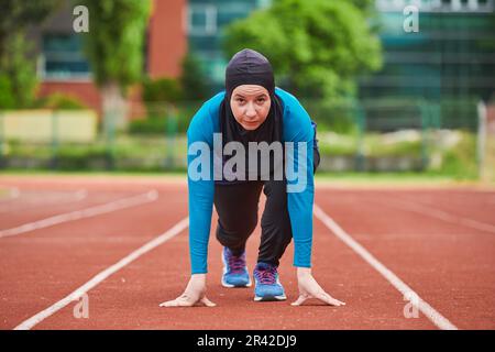 Muslimische Frau in Burka in sportlicher muslimischer Kleidung in Startposition zum Laufen Stockfoto