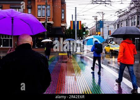 Menschen mit Sonnenschirmen, die an regnerischen Tagen im Castro District, San Francisco, Kalifornien, über den Rainbow Crosswalk spazieren Stockfoto