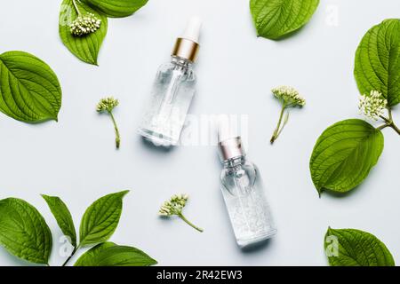 Kosmetische Flüssiggelprodukte und grüne Blätter auf blauem Hintergrund. Beauty-Hautpflegekonzept Stockfoto
