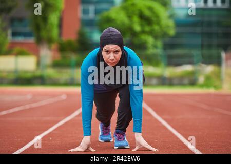 Muslimische Frau in Burka in sportlicher muslimischer Kleidung in Startposition zum Laufen Stockfoto