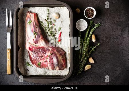 Rohe frische Lammfleisch in Backblech, Kräuter und Gabel auf schwarzen Stein Hintergrund Stockfoto