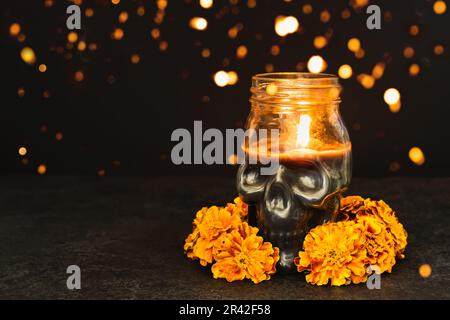 Brennende Kerze Schädel mit Tamponblumen und Bokeh-Lichtern auf schwarzem Hintergrund. Dia de los muertos Tag oder Tag der Toten Stockfoto