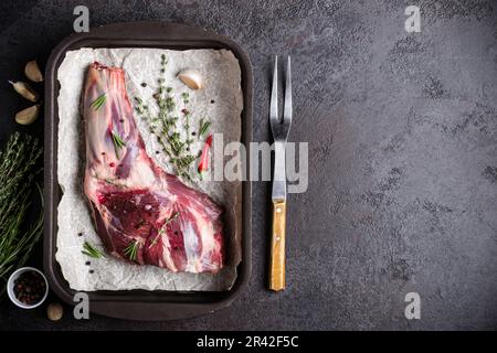 Rohes, frisches Lammfleisch, Kräuter und Gabel auf schwarzem Steinhintergrund Stockfoto