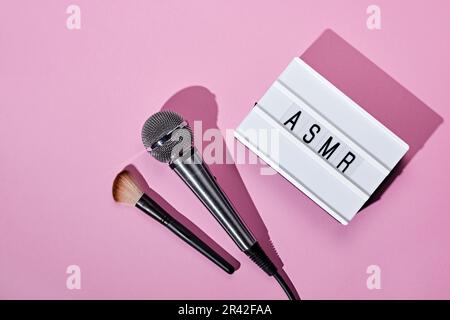 Leuchtkasten für Mikrofon, Pinsel und ASMR-Text auf pinkfarbenem Hintergrund. ASMR-Aufzeichnung Stresslindernde Töne Konzept, flach liegend, Trenddarstellung Stockfoto