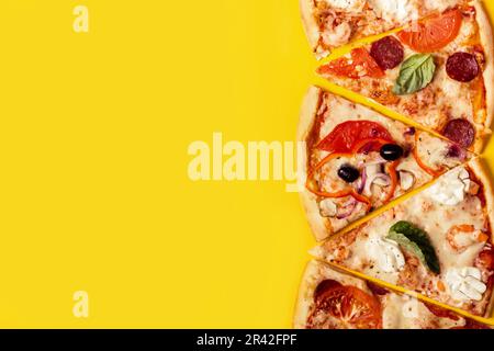Auswahl an Pizzastücken auf gelbem Hintergrund. Pepperoni, vegetarische und Meeresfrüchte-Pizza Stockfoto