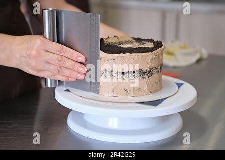 Die Frau, die Konditorin ist, stellt Schokoladencreme auf Schokoladenkuchen, Nahaufnahme. Kuchenzubereitung, selektiver Fokus Stockfoto