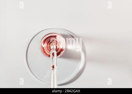 Öl- oder Serumflasche und Pipette in Petrischale auf grauem Hintergrund. Rosafarbenes Kosmetikprodukt Stockfoto