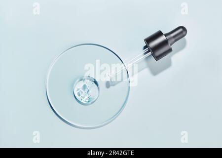 Pipettieren Sie mit einer Probe des kosmetischen Gels in einer Petrischale auf blauem Hintergrund und harten Schatten Stockfoto