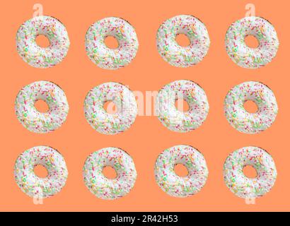 Muster aus Ringdonuts mit weißer Glasur und hunderttausend klatschigen Farben auf orangefarbenem Hintergrund Stockfoto