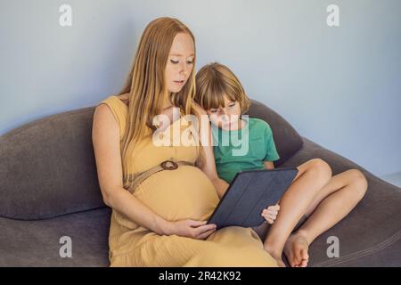 Schwangere mutter und Sohn sehen sich die Tablette an. Ein Buch lesen, einen Cartoon ansehen oder einen Videoanruf tätigen. Sehen Sie sich das Foto vom Ultraschall an Stockfoto