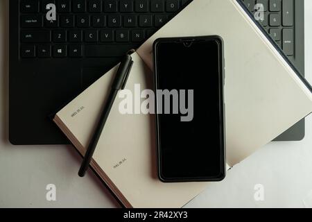 Flaches Bürodesign mit leerem Bildschirm, Mobiltelefon auf weißem Hintergrund, Stift, Laptop und Buch Stockfoto