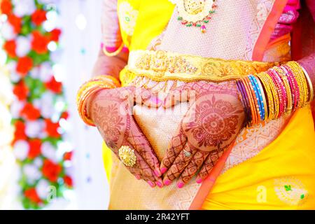 Eine Frau in einem gelben Saree hält ihre Hände in Form ihres Herzens Stockfoto