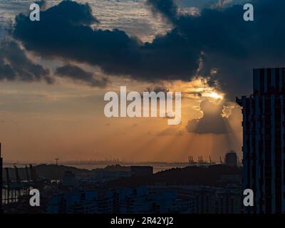 Dunkler und bewölkter Sonnenuntergang in Singapur mit den Konturen des Hafens und der Industriegebiete am Horizont. Stockfoto