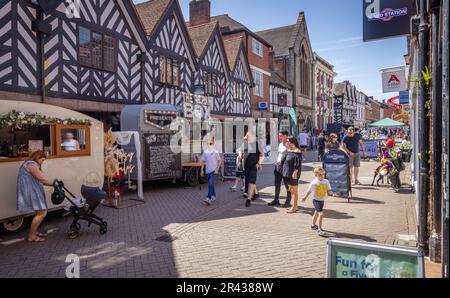 Gäste genießen die Sonne, während sie entlang einer belebten Straße mit Geschäften spazieren und während des Lichfield Food Festivals Speisen und Getränke an den Verkaufsständen aufstellen. Stockfoto