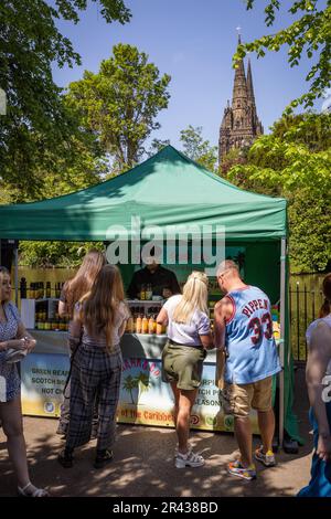 Die Leute versammeln sich beim Lichfield Food Festival an einem Stand. Die Kathedrale von Lichfield ist im Hintergrund zu sehen. Stockfoto