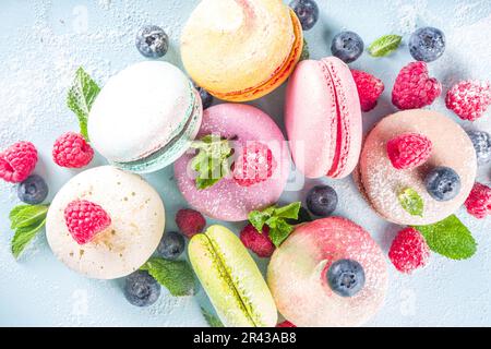 Farbenfrohes französisches Makronen-Dessert. Set von verschiedenen Geschmacksrichtungen und Farbe Makronen-Cookies mit Beeren, Zuckerpulver und Minze auf blauem Hintergrund Stockfoto