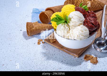 Zitronen-, Schokolade- und Vanilleeis. Große Schüssel mit Eisschaufeln, auf weißem Küchentisch-Hintergrund mit Waffelkegeln, Kopierfläche Stockfoto