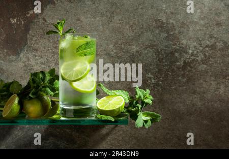 Mojito mit Eis, Limette und Minze. Eisgetränk in einem beschlagenen Glas auf einem alten Steinhintergrund. Speicherplatz kopieren. Stockfoto