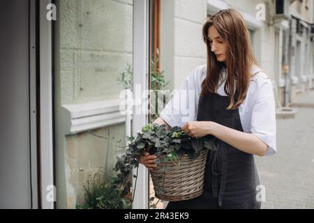 Blumenmädchen mit Efeu in der Nähe eines Blumenladens. Stockfoto