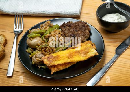 Risoni Pasta - Linsen und Kichererbsen mit veganem Soja-Burger, gebratener Zucchini und Salat Stockfoto