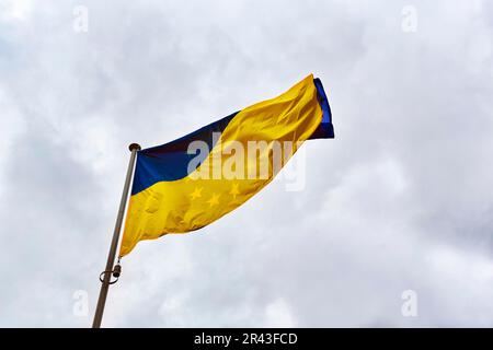 Die europäische Flagge scheint durch die ukrainische Flagge, flattert im wolkigen Himmel, Symbol, EU, Frankreich Stockfoto