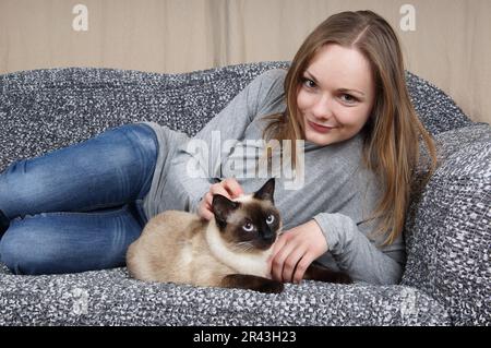Glückliche junge Frau mit siamesischer Katze Stockfoto