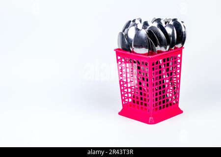 Stapel Metalllöffel in einem rosafarbenen Kunststoffkorb isoliert auf weißem Hintergrund Stockfoto