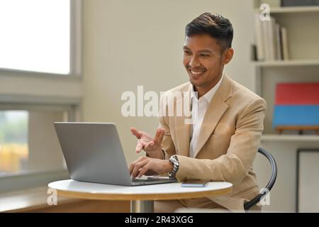 Attraktiver Geschäftsmann in elegantem Anzug, der per Laptop mit einem Geschäftspartner telefoniert Stockfoto