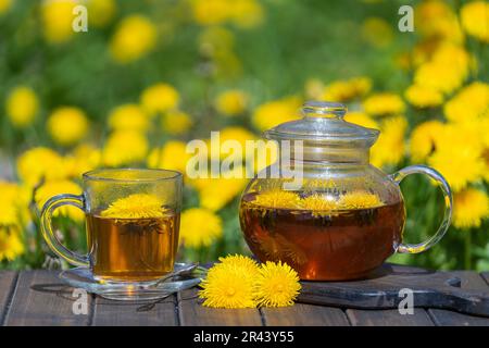 Gesunder Löwenzahn-Blumentee in einer Glasteekanne auf dem Holztisch im Frühlingsgarten, Nahaufnahme Stockfoto