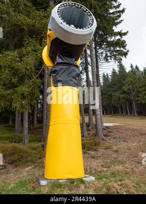 Leuchtend gelbe Schneekanonen am Rande des Hügels mit Blick auf das Tal im Frühling, Berggipfel mit leichter Schneebedeckung im Hintergrund, Stockfoto