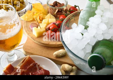 Vorspeise mit kaltem Bier und verschiedenen Fast Food-Gerichten wie Käse, Marmelade, Tomaten, Kartoffeln, Erdnüsse auf weißem Tisch. Erhöhte Aussicht. Stockfoto