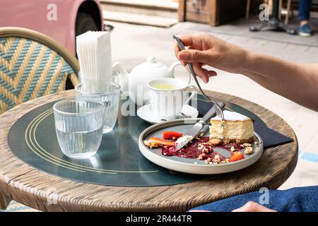 Junge Frau isst Käsekuchen in einem Straßencafé. Stockfoto