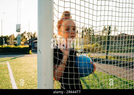 Das Porträt eines Mädchens, das einen Fußball hält, stand bei einem Tor Stockfoto